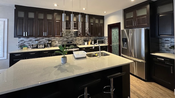 A modern kitchen with dark wood cabinets, stainless steel appliances, and a central island with bar stools.