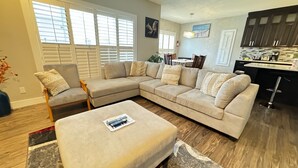 A modern living room with a sectional sofa, a small ottoman, and a dining area with a table and chairs.