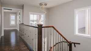 A spacious hallway with a wooden staircase and a modern chandelier.