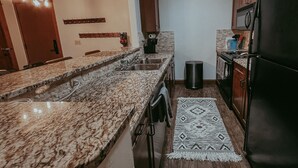 A kitchen with granite countertops, a black refrigerator, wooden cabinets, a sink, and a patterned rug.