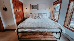 A bedroom with a bed, wooden bench, two framed pictures, and a window.