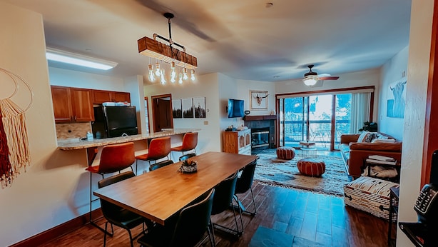 A spacious living area with a dining table, red chairs, a fireplace, and a large window offering a view of the outdoors.