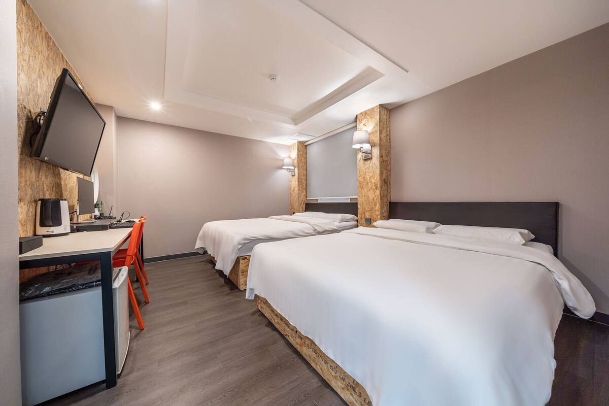 A hotel room with a desk, two beds, a television, and a small refrigerator.