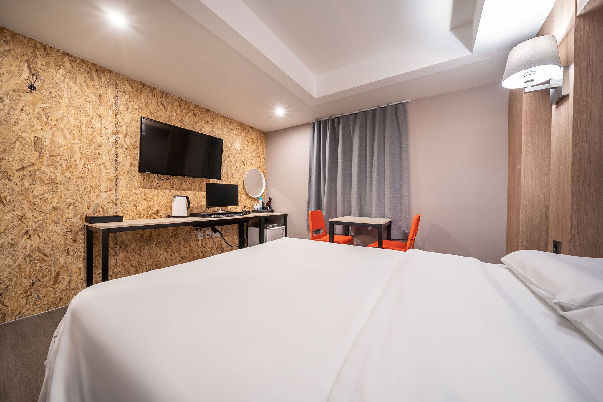 Habitación de hotel con una cama grande, un escritorio con televisor de pantalla plana, una mesita, una silla y una lámpara de pared.