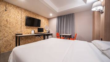 Habitación de hotel con una cama grande, un escritorio con televisor de pantalla plana, una mesita, una silla y una lámpara de pared.