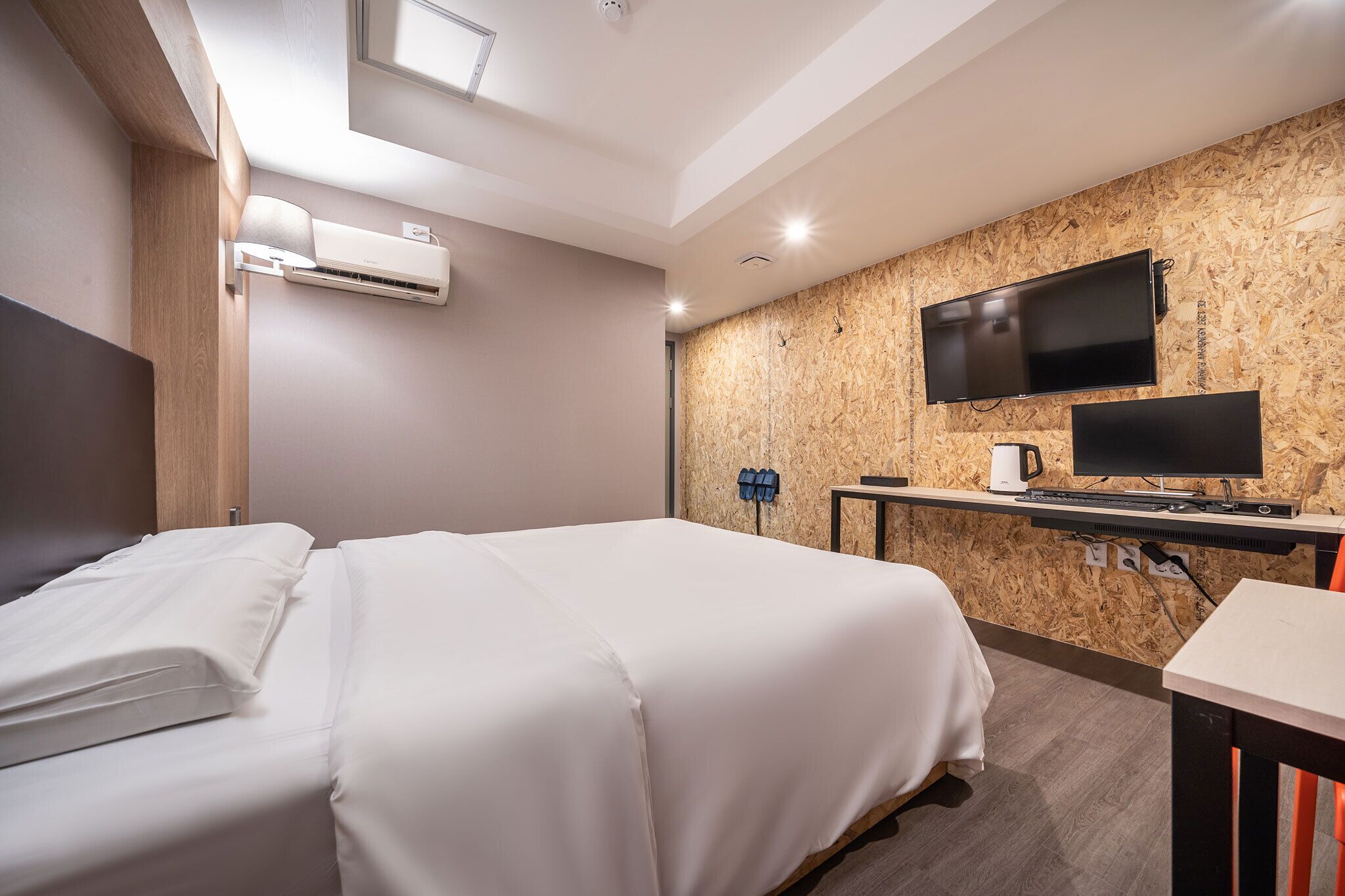 Habitación de hotel con cama, escritorio, televisor de pantalla plana, equipo de aire acondicionado y un panel de pared de madera.