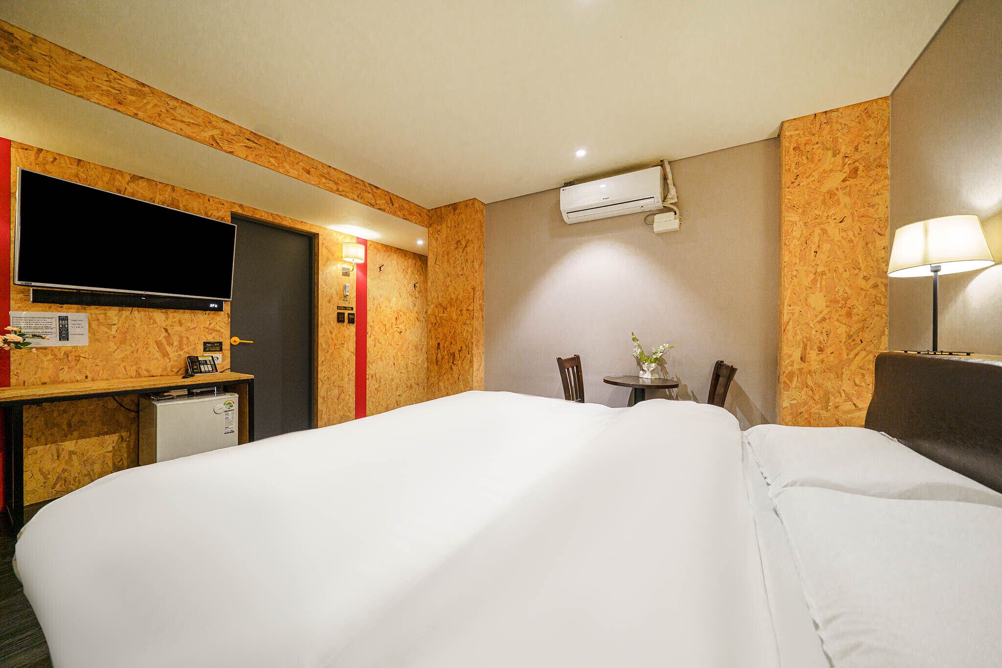 Habitación de hotel con una cama grande, un escritorio con televisión de pantalla plana, un refrigerador pequeño y una lámpara de escritorio.