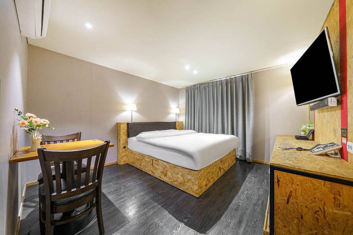 A hotel room with a wooden bed, a desk with a chair, a TV, and a telephone.