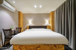 Quarto de hotel com uma cama grande, duas luminárias de cabeceira, um painel de madeira na cabeceira, uma mesinha com cadeiras e um aparelho de ar condicionado.