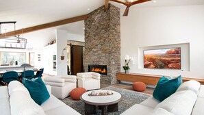 Ein modernes Wohnzimmer mit Kamin aus Stein, weißen Sofas und einem großen Fernseher an der Wand.