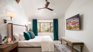 Ein Schlafzimmer mit einem Bett, Nachttischen, einer Bank, einem Deckenventilator und einem großen Fenster mit Vorhängen.