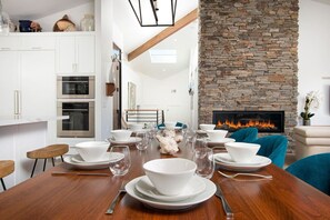 Une cuisine moderne avec des meubles blancs, une cheminée en pierre et un coin repas aménagé pour accueillir six personnes.