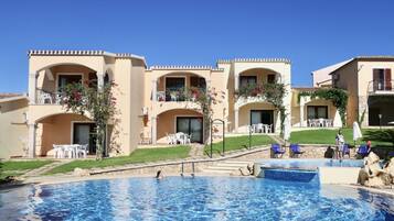 A hotel with a swimming pool, multiple balconies with outdoor seating, and a clear blue sky.