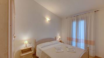Quarto com cama, luminárias de cabeceira, mesa de cabeceira e janela com cortinas.