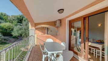 Un balcon avec une table et des chaises, une porte vitrée donnant sur un coin repas et une vue sur la verdure.