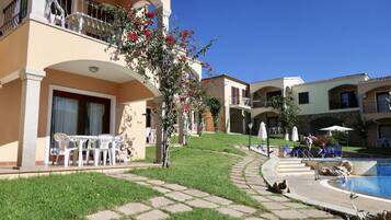 A hotel courtyard with a swimming pool, outdoor seating, and a well-maintained lawn.