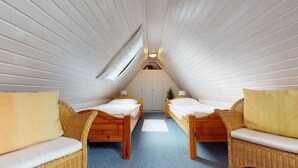 A cozy attic bedroom with two wooden beds, wicker furniture, and a sloped ceiling.