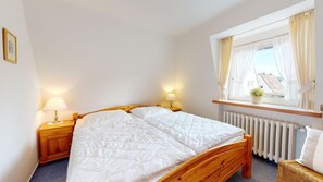 Um quarto com uma cama de madeira, duas mesas de cabeceira com abajures, uma janela com cortinas e um radiador.