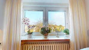 A window with a view of a landscape, a radiator below, and three potted plants on the windowsill.
