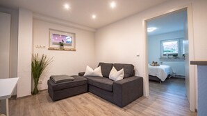 Una sala de estar moderna con un sofá seccional gris, una mesita y una planta. Se ve un ventanal con vistas a zonas verdes.