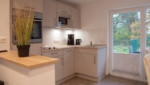 Una cocina moderna con armarios blancos, microondas, cafetera y una planta en maceta.