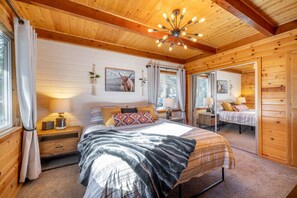 A cozy wooden cabin bedroom with a large bed, bedside tables, and a ceiling light fixture.