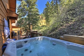A hot tub in a wooden deck area with a view of a forested hillside.