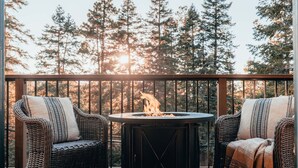 Un balcon avec des fauteuils en osier et une table ronde autour d’un foyer.