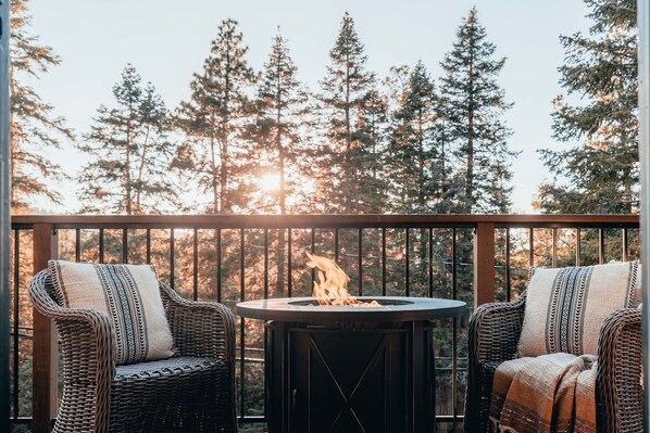 A balcony with wicker chairs and a round table with a fire pit.