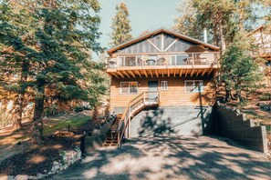 A two-story wooden cabin with a balcony, surrounded by trees.