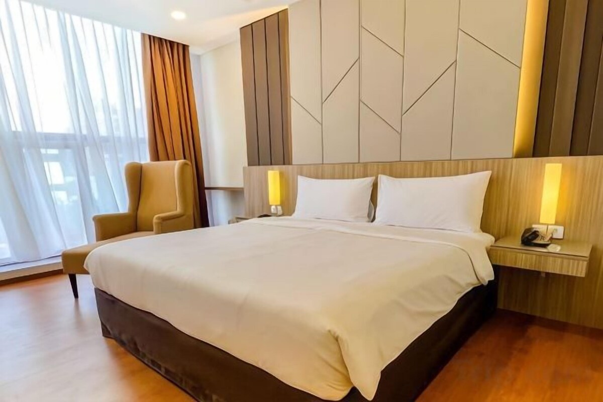 A hotel room with a large bed, bedside tables, a chair, and a view of the outdoors.
