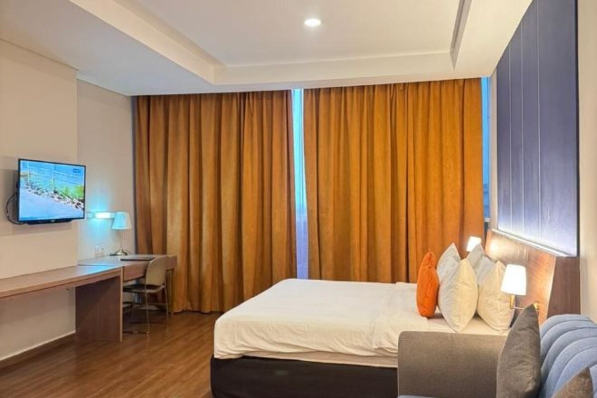 A hotel room with a bed, a desk, a television, and curtains.