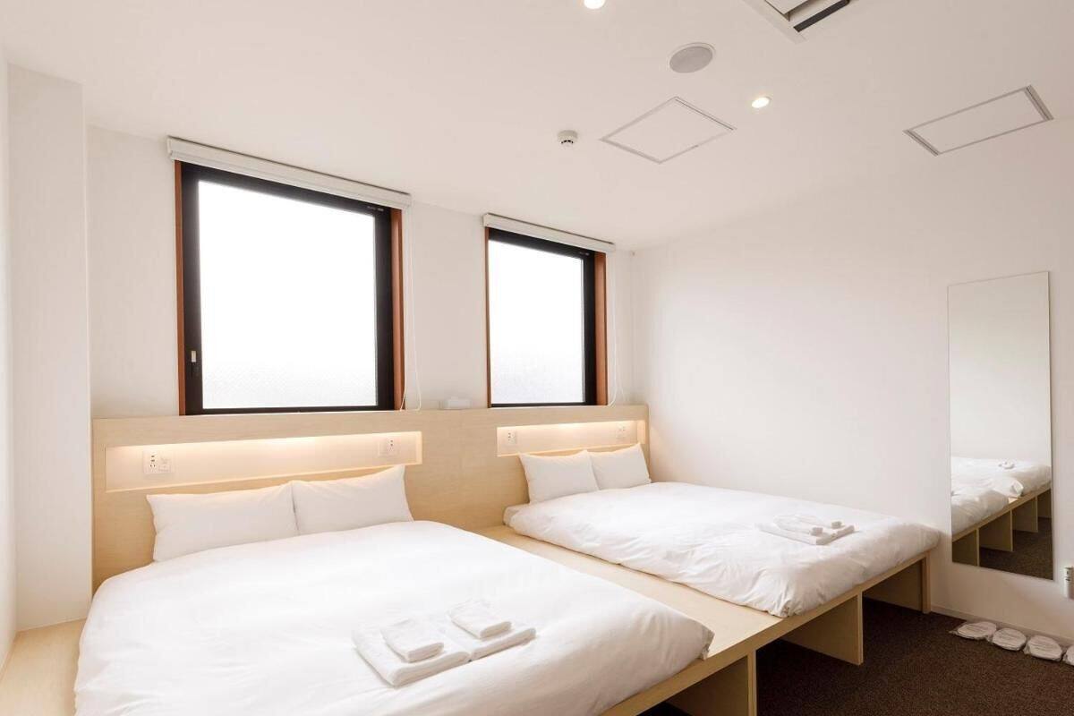A hotel room with two single beds, a large mirror, and a window with blinds.