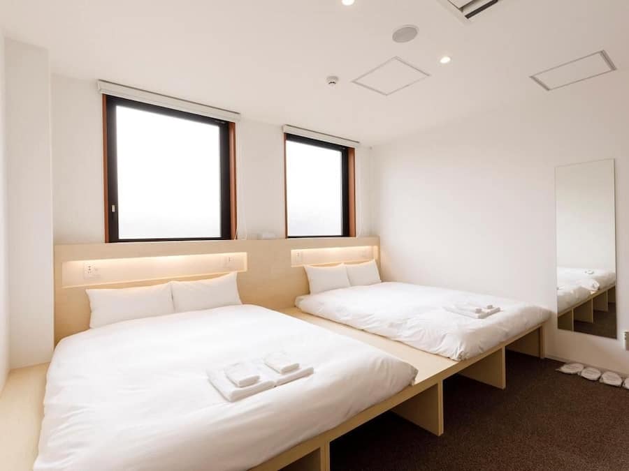A hotel room with two single beds, a large mirror, and a window with blinds.