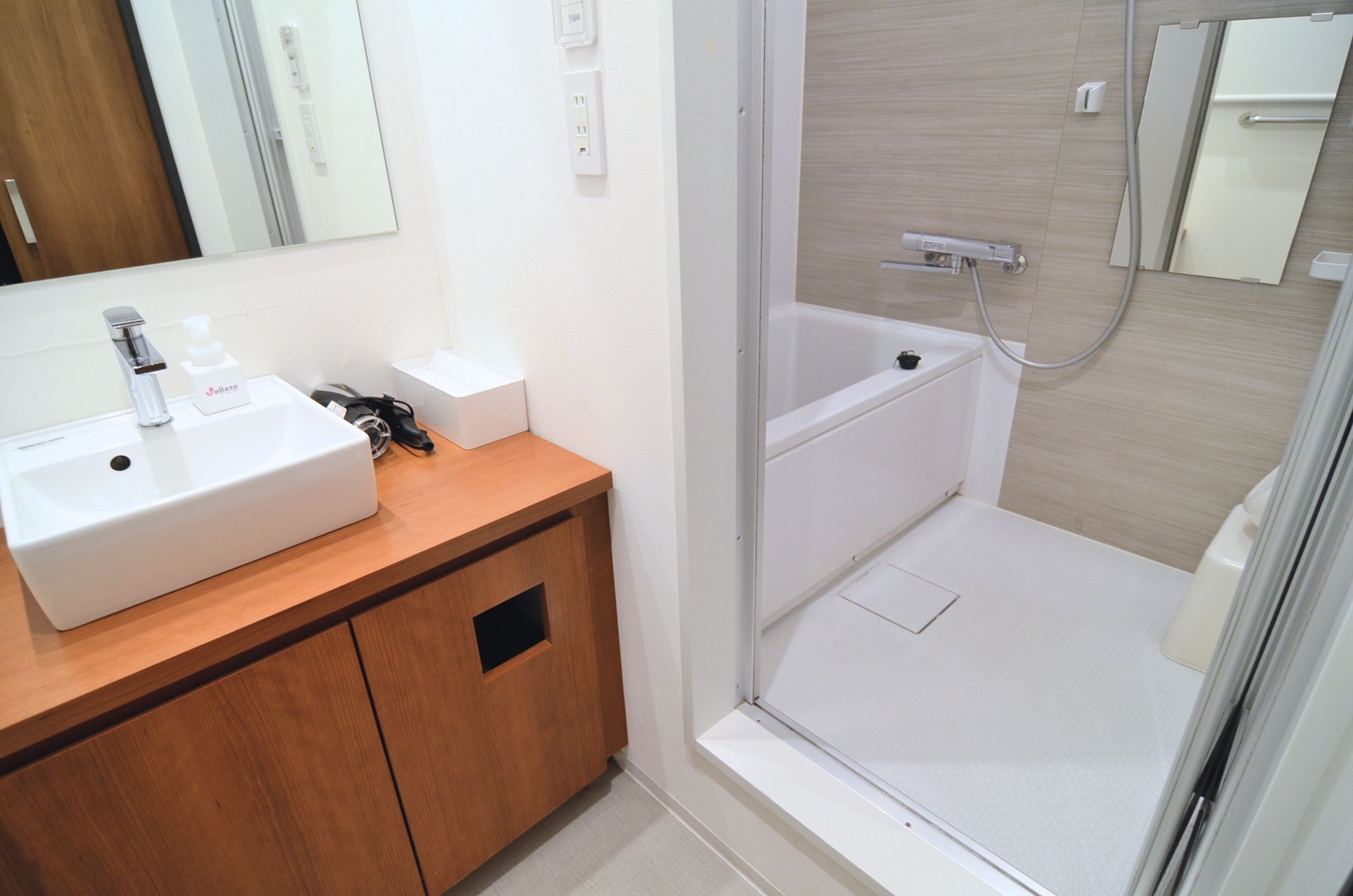 A bathroom with a white sink, wooden vanity, a mirror, and a shower area.
