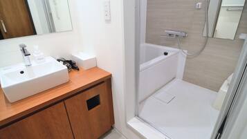 A bathroom with a white sink, wooden vanity, a mirror, and a shower area.