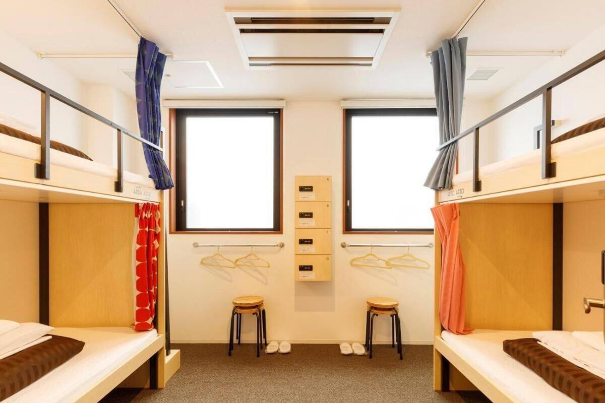 A dormitory room with bunk beds, a small seating area, and a window.