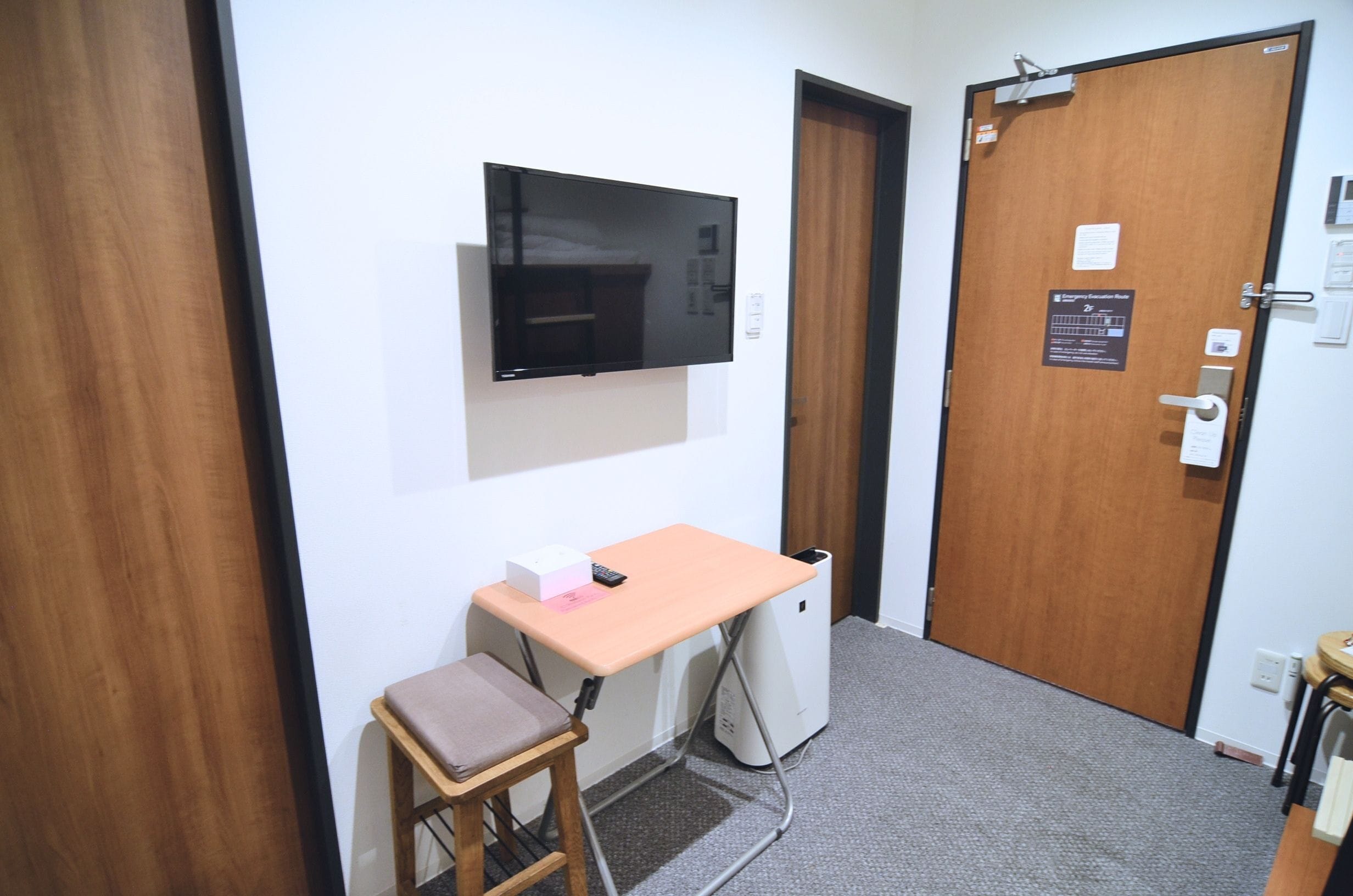 A small room with a desk, chair, and a television mounted on the wall.
