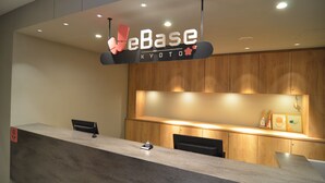 Un mostrador de recepción con un letrero que dice 'eBase Kyoto', paneles de madera y una lámpara de escritorio pequeña.