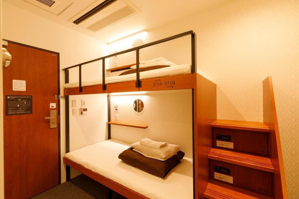 A bunk bed room with a wooden door, a small shelf, and a wall-mounted light.