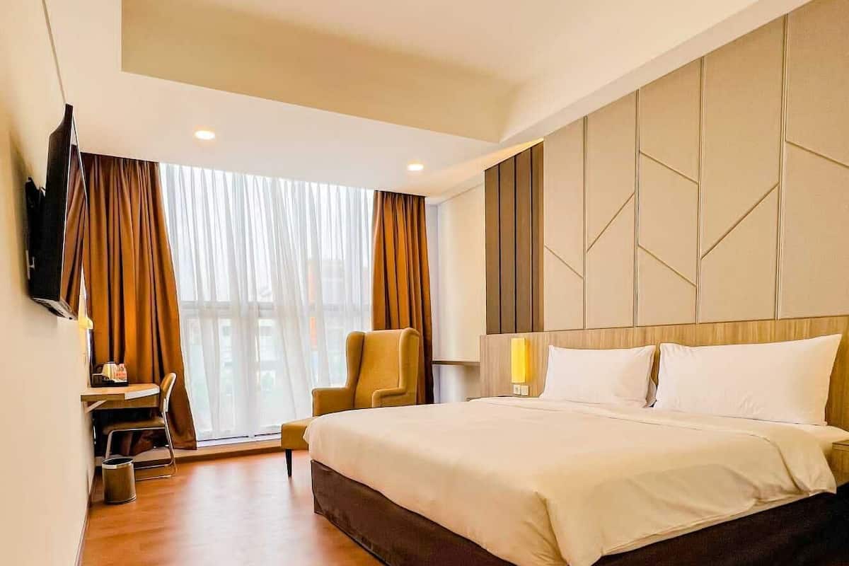A hotel room with a large bed, a desk, a chair, and a TV mounted on the wall.