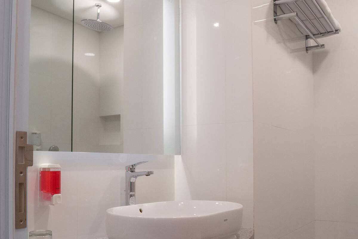 A modern bathroom with a white sink, a large mirror, and a shower area.