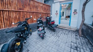 Ein gepflasterter Innenhof mit drei parkenden Motorrädern vor einem Bambuszaun.