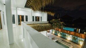 Ein modernes Gebäude mit einem Strohdach, einem Swimmingpool und einem gut beleuchteten Außenbereich mit Pflanzen.
