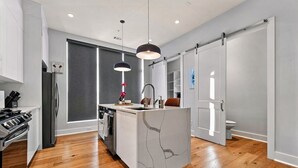 A modern kitchen with a central island, wooden flooring, and a large window. - Spacious 3BR Townhome with Majestic Rooftop Views (Atlanta)