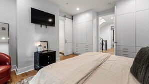 A bedroom with a bed, a TV mounted on the wall, a dresser, and a closet. - Spacious 3BR Townhome with Majestic Rooftop Views (Atlanta)