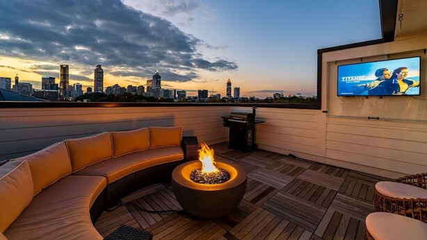 A rooftop terrace with a curved sofa, a fire pit, and a TV screen displaying 'Titanic'. - Spacious 3BR Townhome with Majestic Rooftop Views (Atlanta)