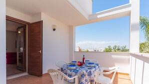 An outdoor balcony with a table set for dining, white chairs, and a view of the cityscape.