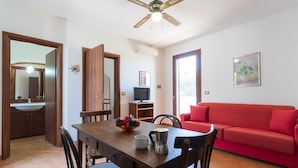 A dining area with a wooden table, chairs, a red sofa, and a ceiling fan.