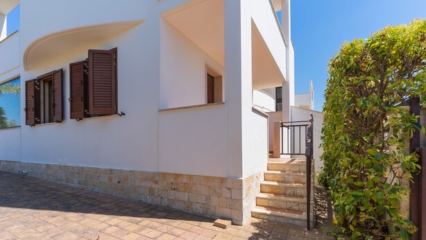 A white building with brown shutters, a stone base, and a staircase leading to an upper level.
